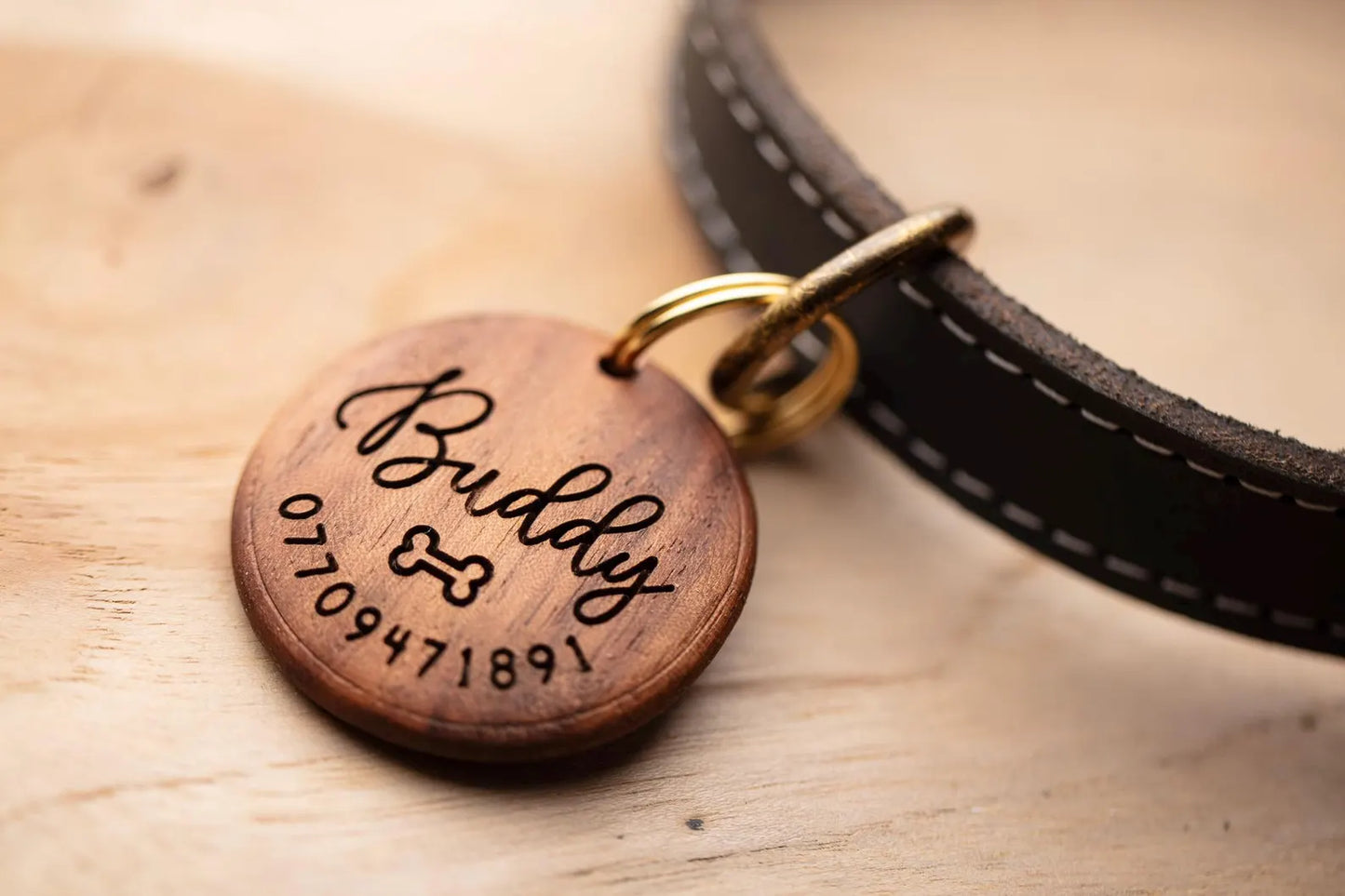 Wooden pet tag with engraved text on a leather collar, placed on a wooden surface.