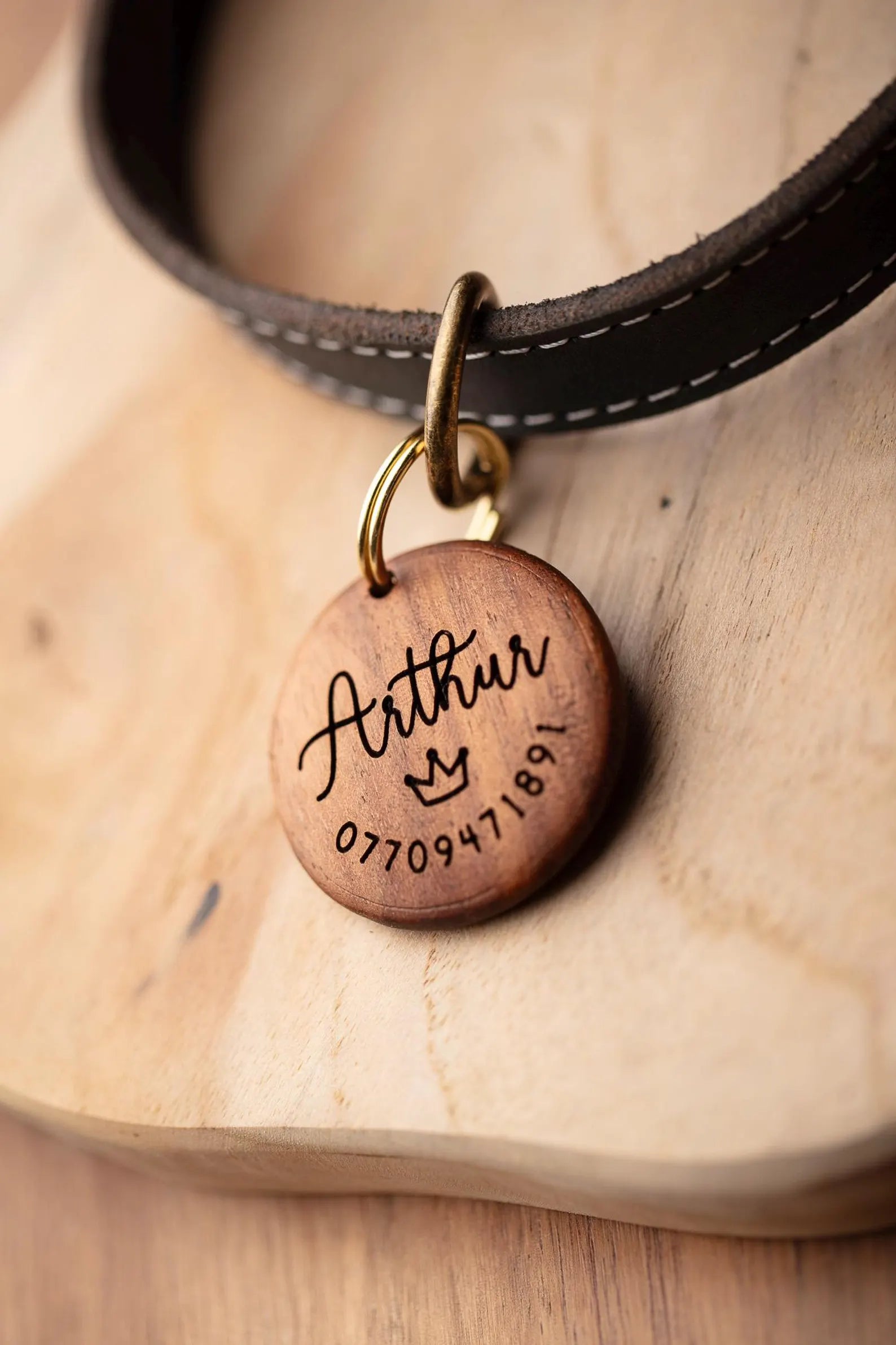 Wooden pet tag with engraved name and number on a leather collar.